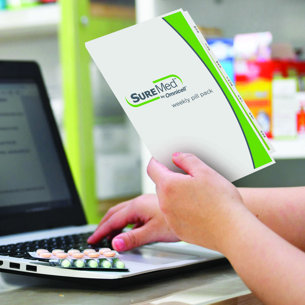 Pharmacist holding the SureMed pack and entering information on his laptop